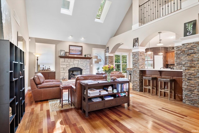 living room with light hardwood / wood-style flooring, a skylight, high vaulted ceiling, and a stone fireplace