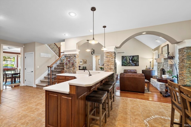 kitchen featuring a breakfast bar area, decorative light fixtures, a fireplace, light tile patterned floors, and decorative columns