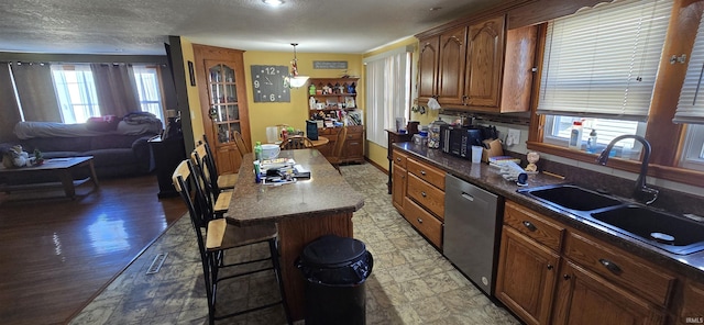 kitchen with dark countertops, a sink, a textured ceiling, dishwasher, and a kitchen bar