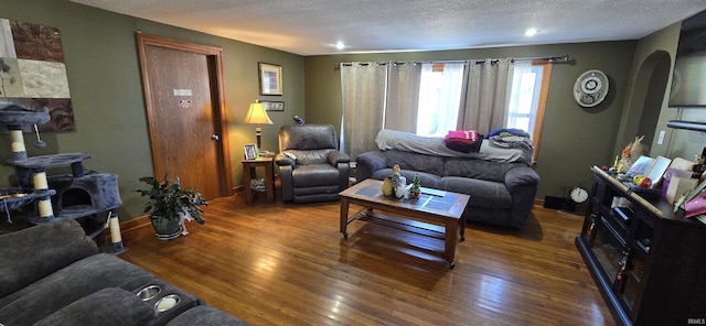 living area featuring a textured ceiling, wood-type flooring, arched walkways, and baseboards