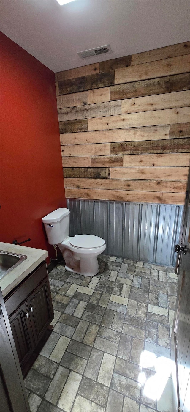 bathroom with vanity, toilet, and wooden walls