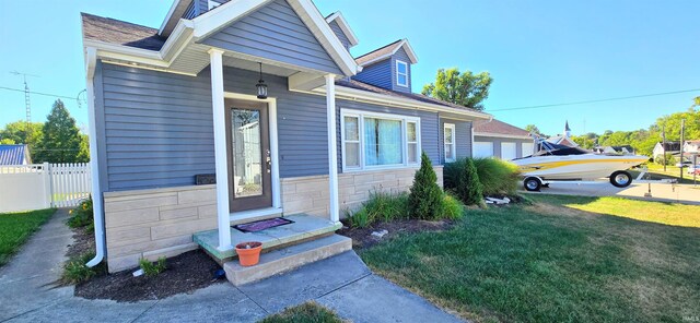 entrance to property featuring a garage, a yard, stone siding, and fence