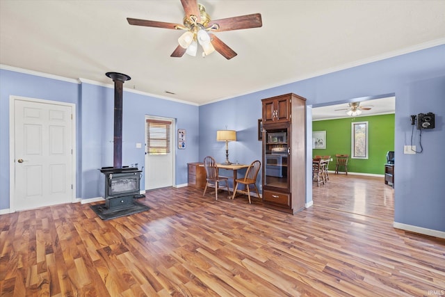 unfurnished living room with a wood stove, crown molding, ceiling fan, and hardwood / wood-style floors