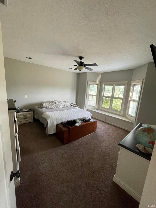 bedroom featuring ceiling fan, a textured ceiling, and dark colored carpet