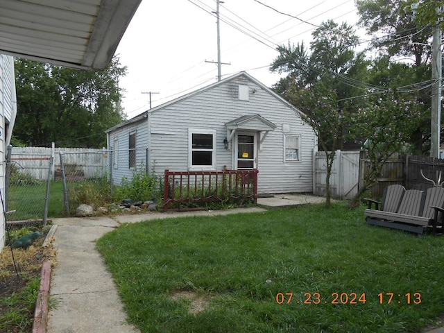 back of house featuring fence, a lawn, and a gate