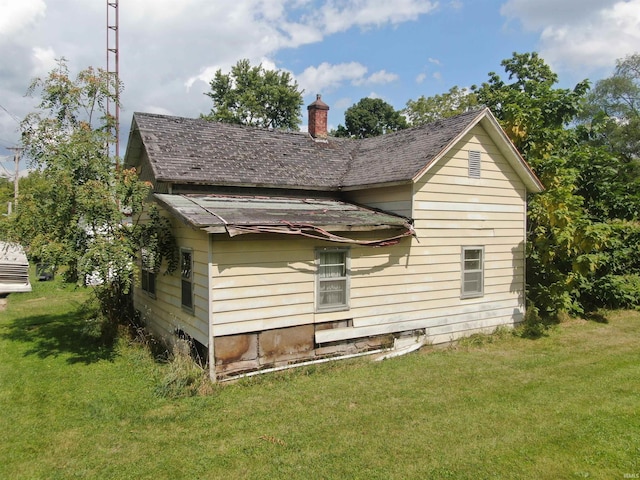 rear view of house featuring a chimney, a yard, and roof with shingles