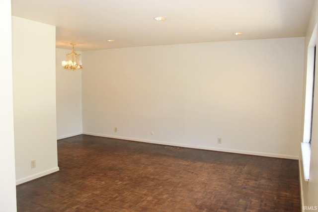 spare room featuring dark parquet floors and a notable chandelier