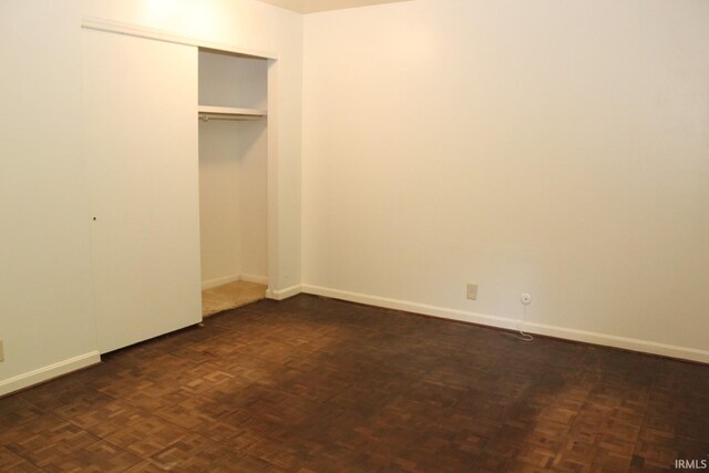 unfurnished bedroom featuring dark parquet floors and a closet