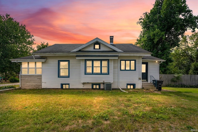 back house at dusk with a lawn and cooling unit