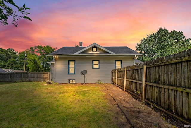 back house at dusk featuring a lawn