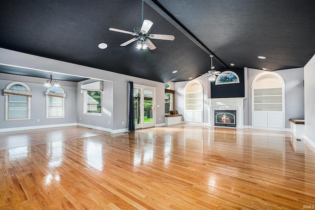 unfurnished living room with beamed ceiling, ceiling fan, built in shelves, and light hardwood / wood-style flooring