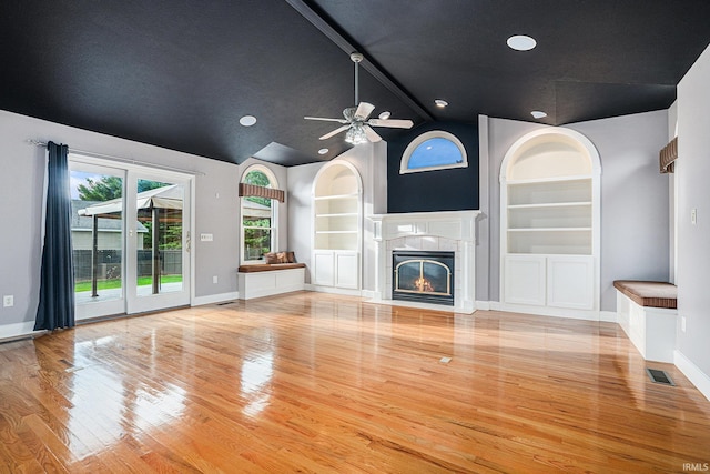 unfurnished living room with light wood-type flooring, a fireplace, vaulted ceiling with beams, ceiling fan, and built in features