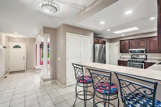 kitchen featuring dark brown cabinets, a textured ceiling, decorative columns, decorative backsplash, and stainless steel appliances