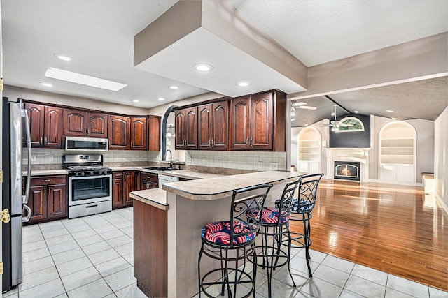 kitchen with sink, kitchen peninsula, appliances with stainless steel finishes, light wood-type flooring, and a kitchen bar