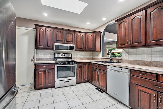 kitchen featuring appliances with stainless steel finishes, decorative backsplash, light tile patterned floors, a skylight, and sink