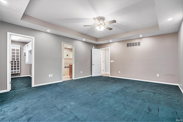 unfurnished bedroom with a tray ceiling, a spacious closet, ceiling fan, and ensuite bathroom