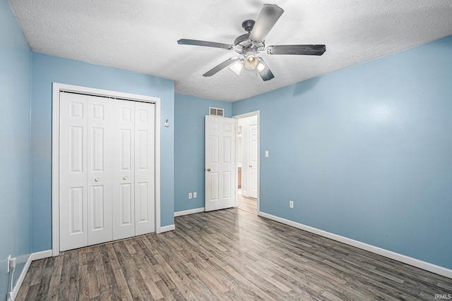 unfurnished bedroom with ceiling fan, a textured ceiling, a closet, and dark hardwood / wood-style floors