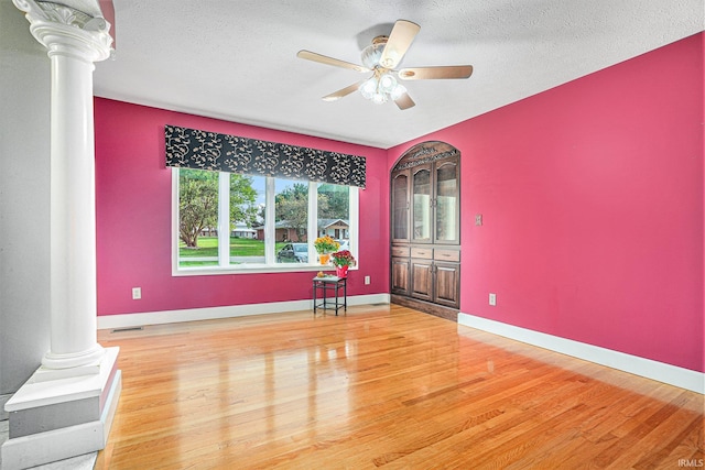 unfurnished room featuring a textured ceiling, hardwood / wood-style floors, ceiling fan, and ornate columns