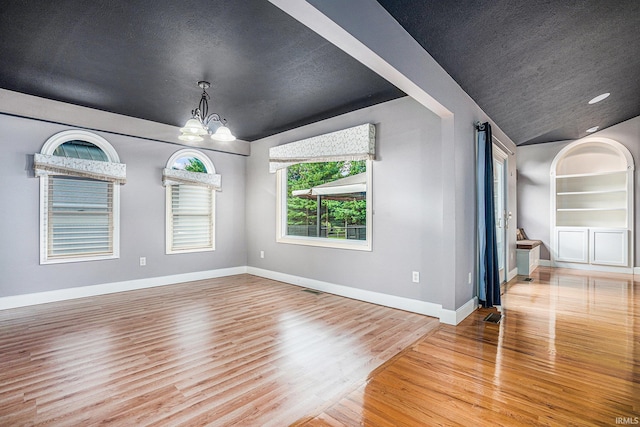 unfurnished living room with light hardwood / wood-style flooring, vaulted ceiling, a textured ceiling, and a notable chandelier