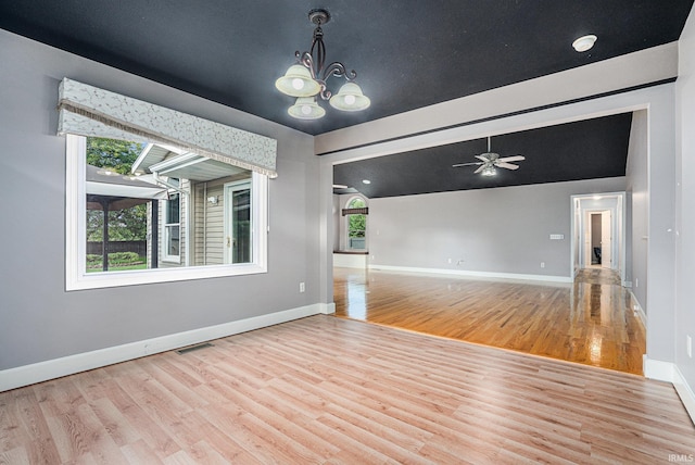 empty room with ceiling fan with notable chandelier, vaulted ceiling, and light hardwood / wood-style floors