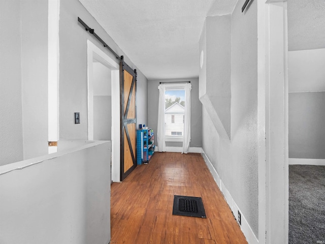 corridor featuring a barn door, wood-type flooring, and a textured ceiling