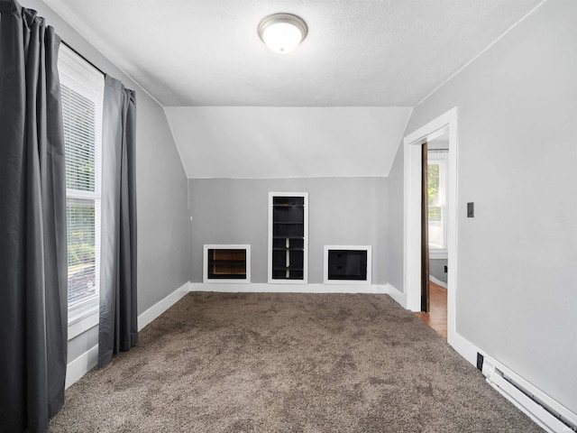 additional living space with a healthy amount of sunlight, baseboard heating, vaulted ceiling, and a fireplace