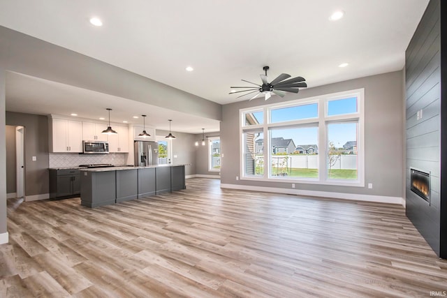 kitchen with a fireplace, appliances with stainless steel finishes, light hardwood / wood-style floors, white cabinetry, and an island with sink