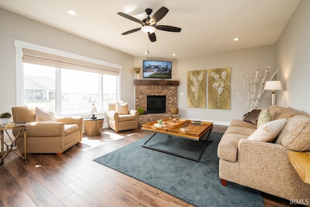 living room featuring a brick fireplace, wood-type flooring, and ceiling fan