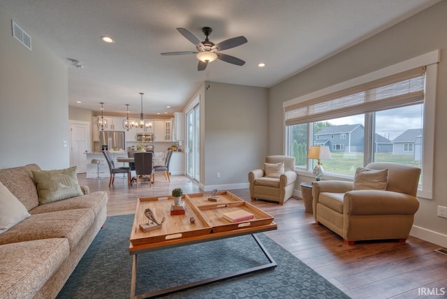 living room with ceiling fan with notable chandelier and light hardwood / wood-style floors