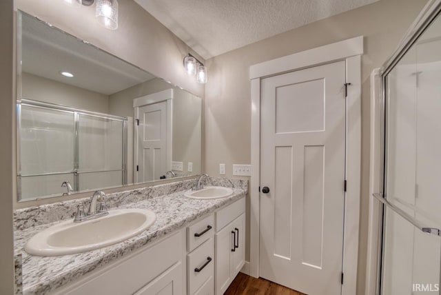 bathroom with a textured ceiling, vanity, an enclosed shower, and hardwood / wood-style flooring