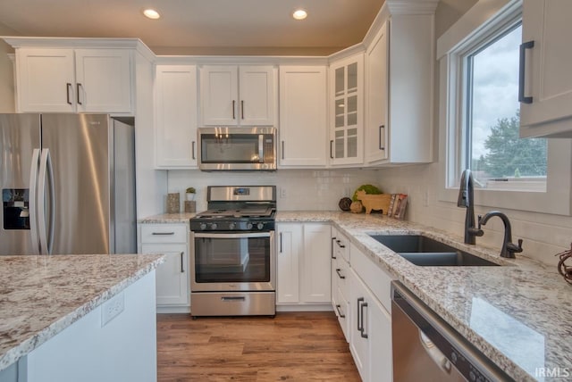 kitchen with light wood-type flooring, sink, light stone countertops, appliances with stainless steel finishes, and white cabinets