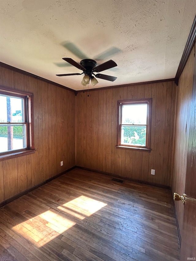 unfurnished room with wooden walls, wood-type flooring, ceiling fan, and a wealth of natural light