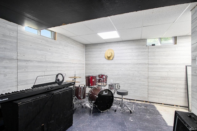 miscellaneous room featuring plenty of natural light, concrete floors, wood walls, and a drop ceiling