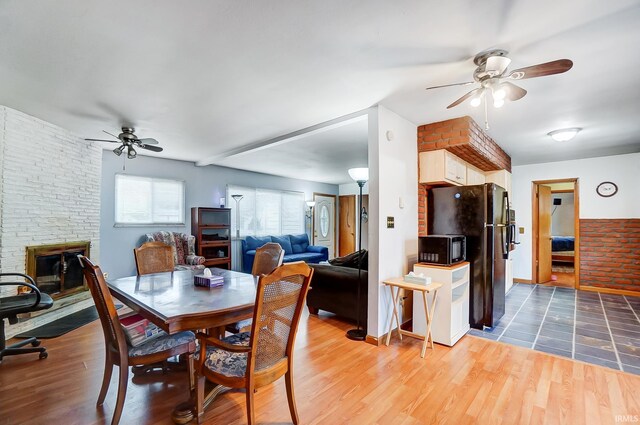 dining space featuring brick wall, ceiling fan, dark hardwood / wood-style flooring, and a stone fireplace