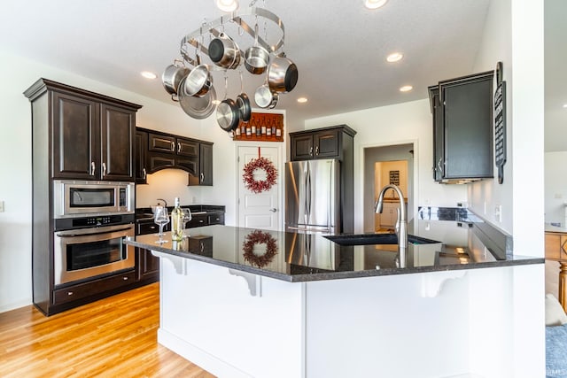 kitchen with appliances with stainless steel finishes, dark brown cabinets, light hardwood / wood-style floors, and sink