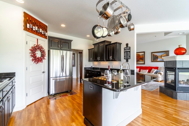 kitchen featuring light wood-type flooring, stainless steel fridge, a breakfast bar, and a tile fireplace