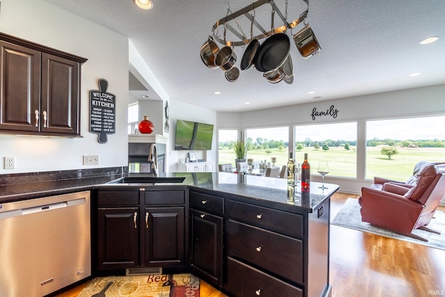 kitchen featuring a textured ceiling, dark brown cabinets, dishwasher, sink, and light wood-type flooring