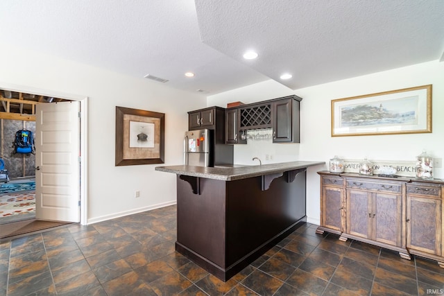 kitchen featuring stainless steel fridge, kitchen peninsula, a textured ceiling, and a breakfast bar