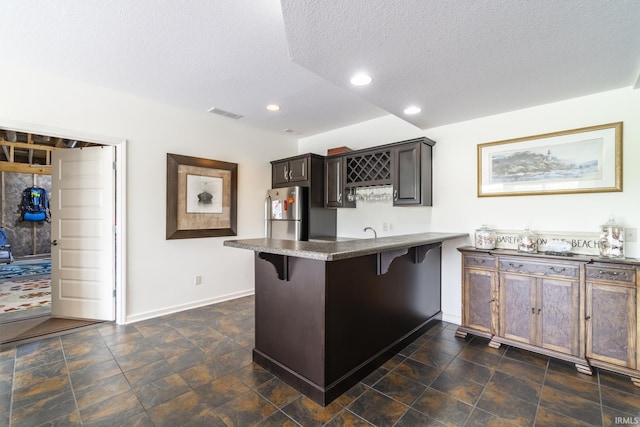 kitchen with a textured ceiling, a breakfast bar, a peninsula, baseboards, and freestanding refrigerator