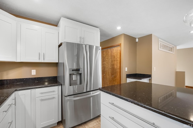 kitchen featuring dark stone countertops, stainless steel fridge, and white cabinets