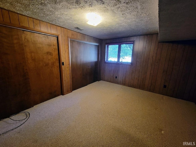 unfurnished bedroom featuring carpet, a textured ceiling, and wood walls