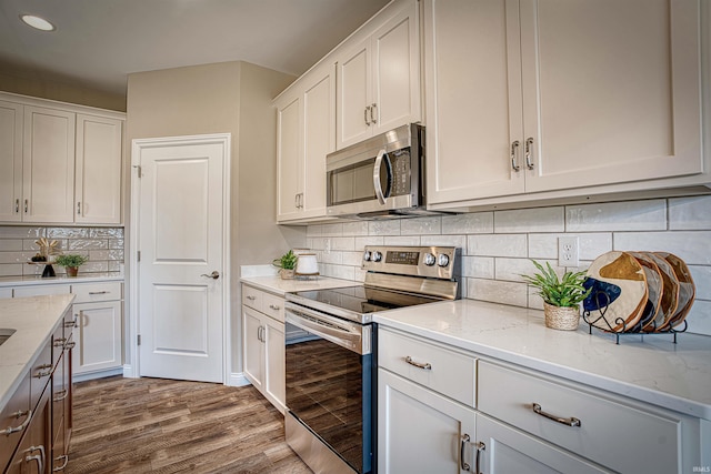 kitchen with white cabinets, appliances with stainless steel finishes, light stone counters, wood-type flooring, and decorative backsplash