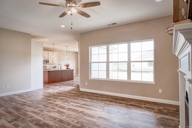 unfurnished living room featuring dark wood-type flooring, ceiling fan, and sink