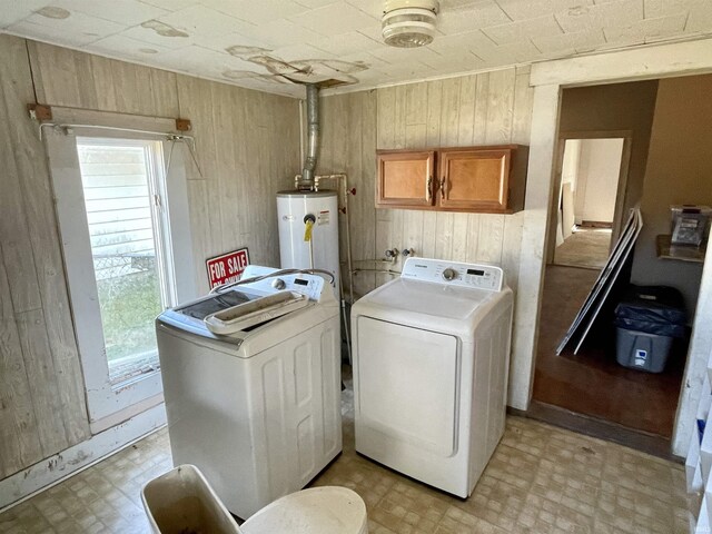 clothes washing area featuring separate washer and dryer, wooden walls, cabinets, and water heater