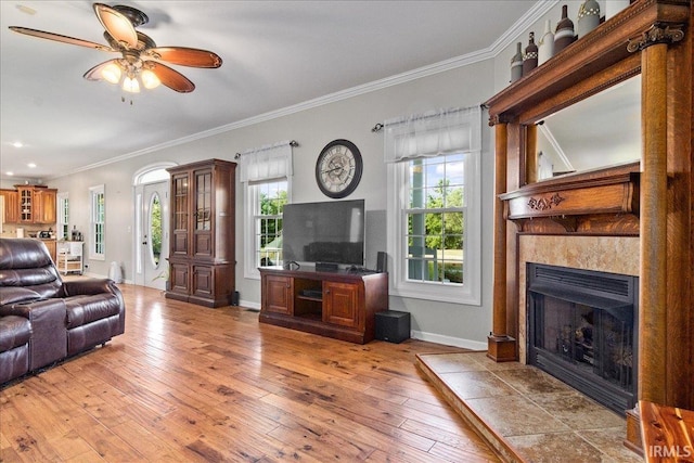 living room featuring crown molding, ceiling fan, light wood-type flooring, and a tile fireplace