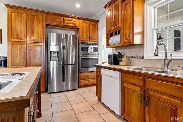 kitchen with light tile patterned floors, tasteful backsplash, stainless steel appliances, sink, and ornamental molding