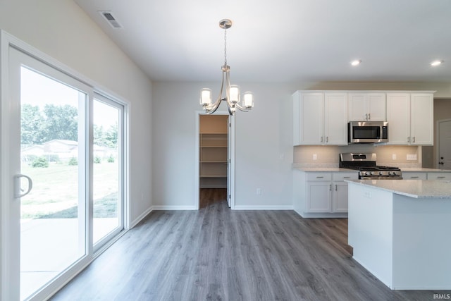 kitchen featuring pendant lighting, hardwood / wood-style floors, backsplash, stainless steel appliances, and white cabinets