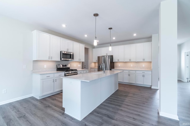 kitchen with white cabinets, appliances with stainless steel finishes, light stone counters, and a center island with sink