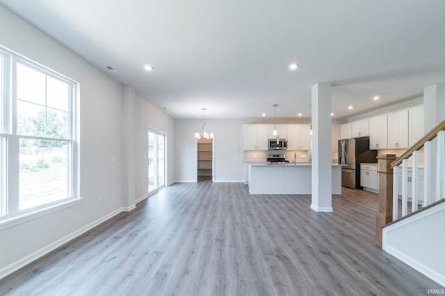 unfurnished living room with light wood-type flooring and an inviting chandelier