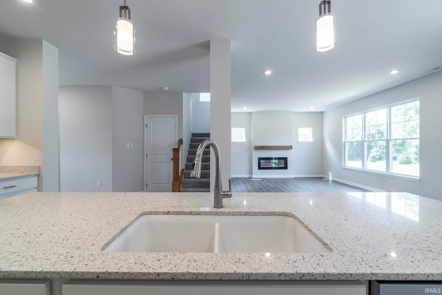 kitchen with pendant lighting, hardwood / wood-style floors, sink, and light stone countertops